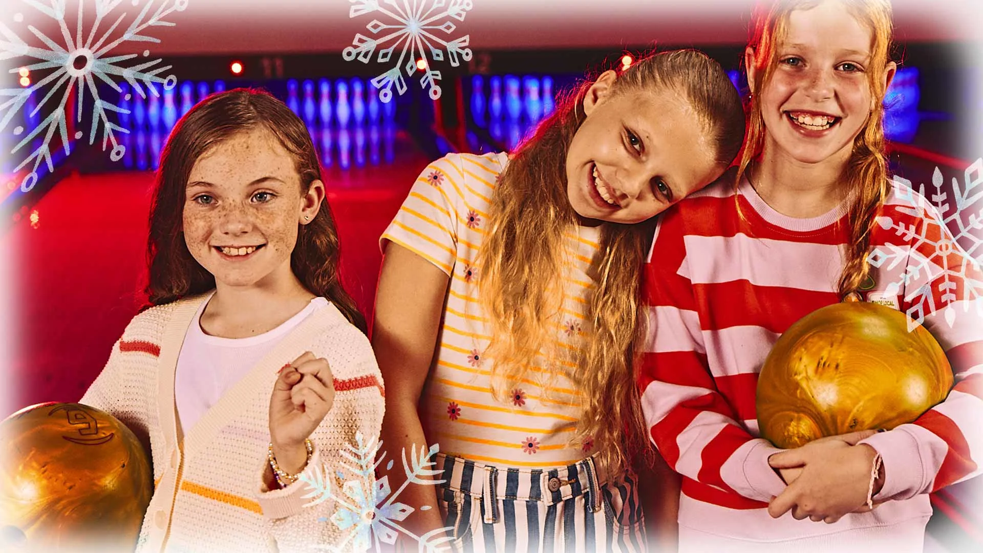 Three kids holding bowling balls with bowling lanes in the background.