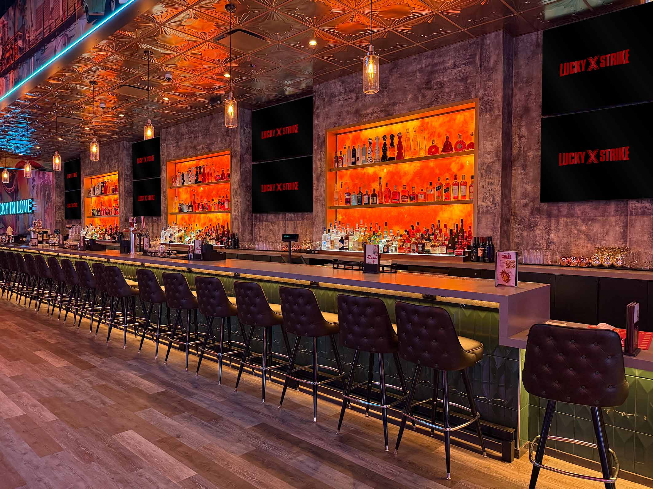 A modern Lucky Strike bar with a long counter, high-top stools, backlit shelves of spirits, and warm ambient lighting.