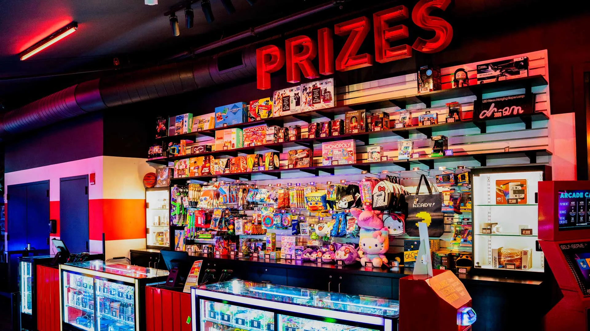 Lucky Strike prize counter filled with colorful arcade rewards, toys, and games beneath illuminated “PRIZES” sign.