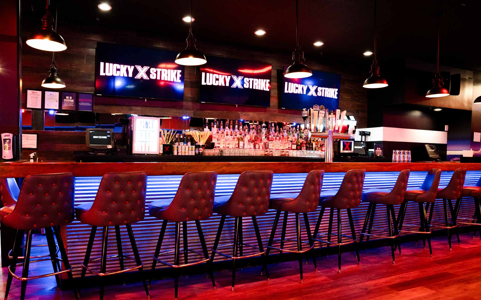 Upscale bar at Lucky Strike bowling alley with leather bar stools, glowing blue underlighting, beer taps, and large digital screens displaying the Lucky Strike logo.
