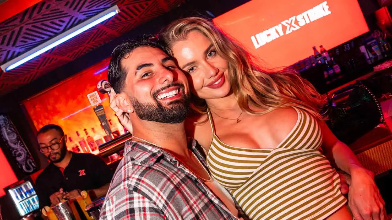 Couple smiling together at the Lucky Strike bar with neon lighting and a glowing Lucky Strike sign in the background