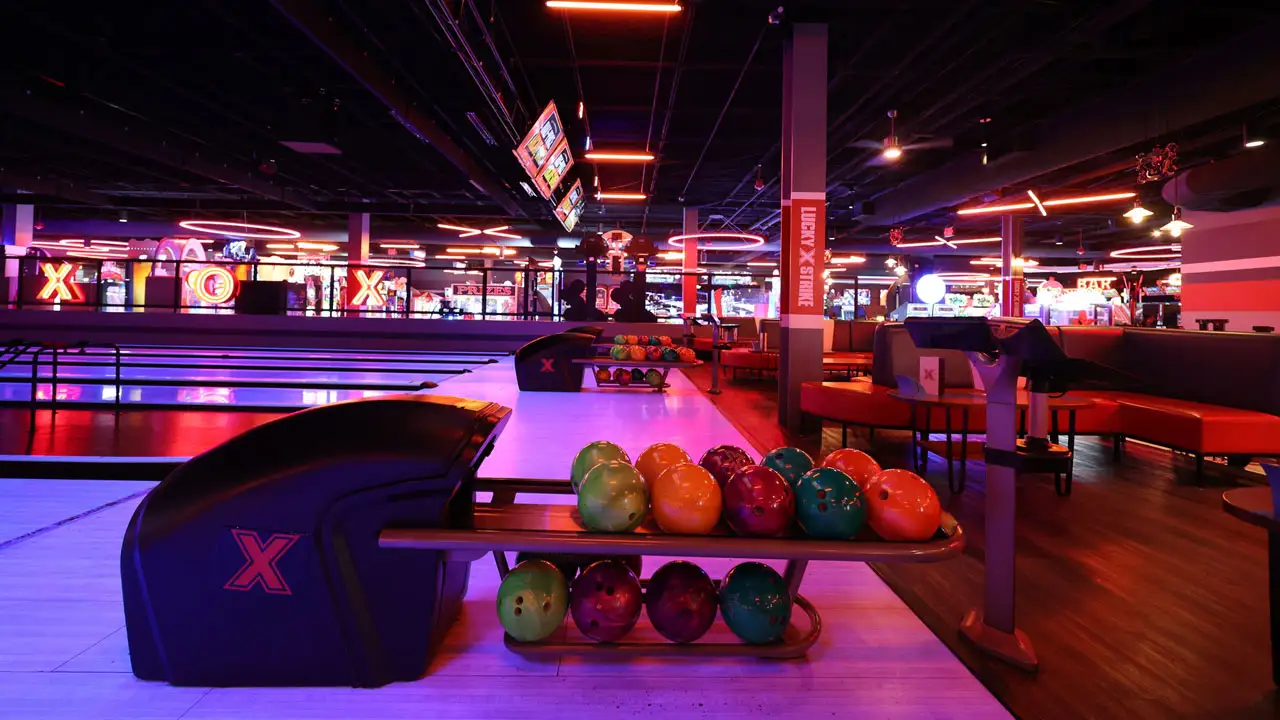 Colorful bowling balls in a return rack with bowling lanes and a large, beautiful bowling center in the background.