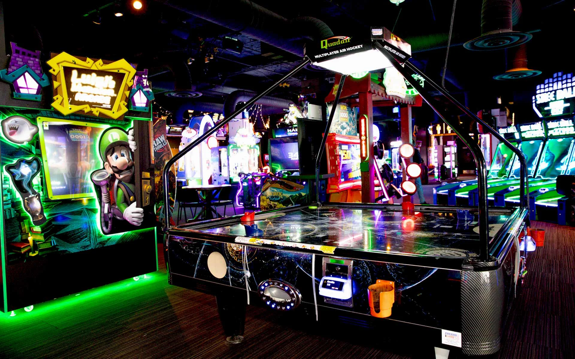 Neon-lit arcade at Lucky Strike featuring multiplayer air hockey table and colorful game machines, including Luigi’s Mansion, in a vibrant entertainment space.
