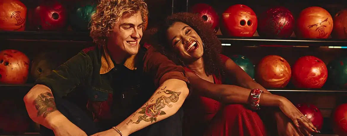 Two people having fun and smiling while sitting in front of bowling balls