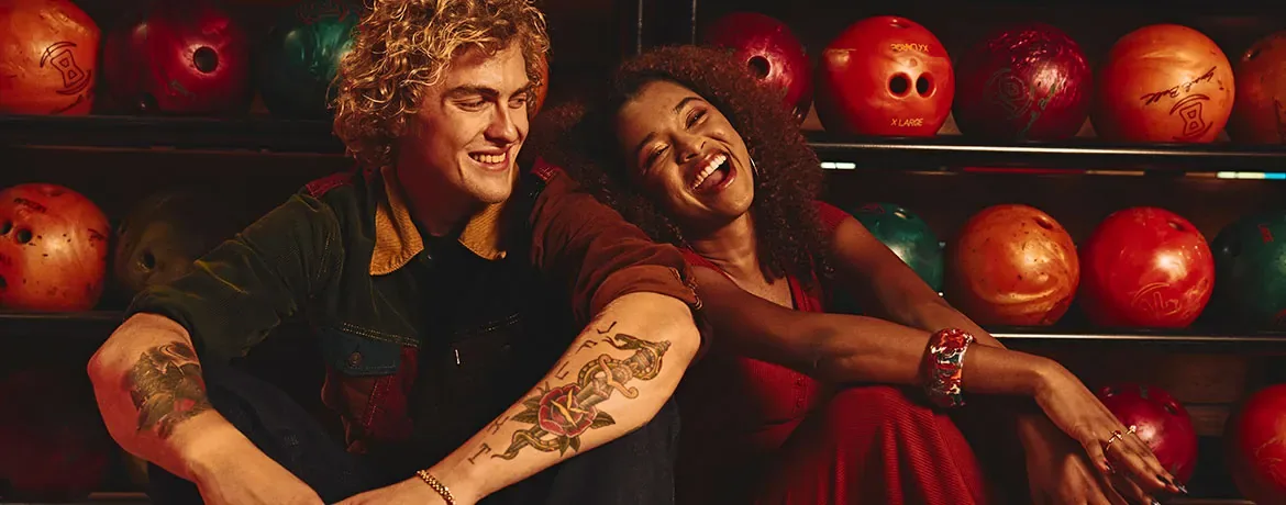 Two people having fun and smiling while sitting in front of bowling balls
