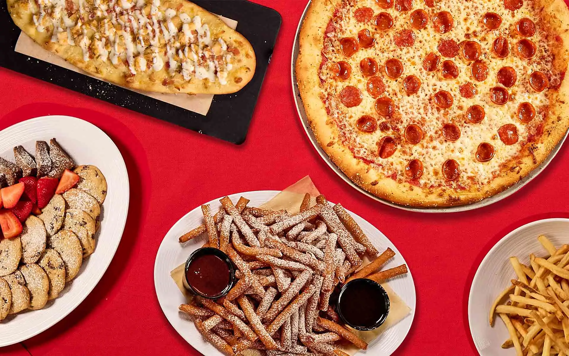 Delicious pepperoni pizza, flat bread, french fries, and sweet deserts on a holiday themed table.