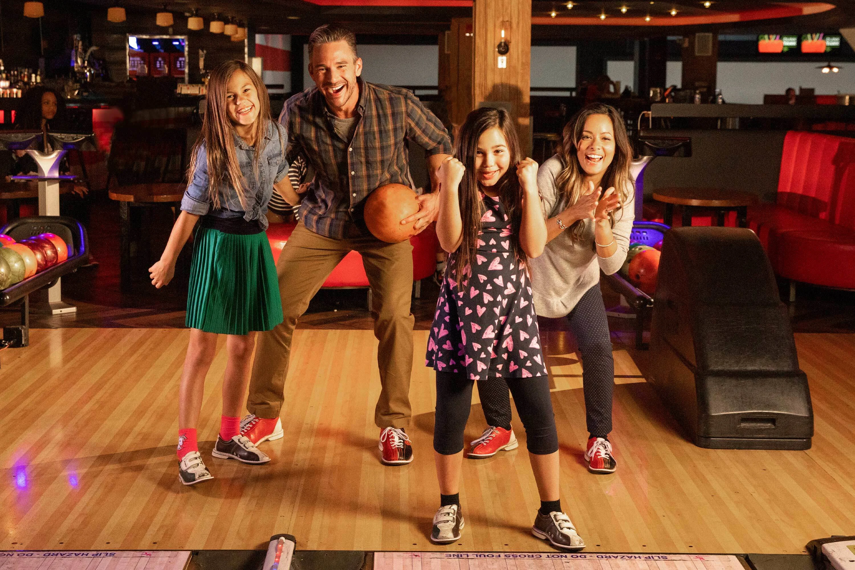 A family bonding on the lanes holding bowling balls and cheering each other on.