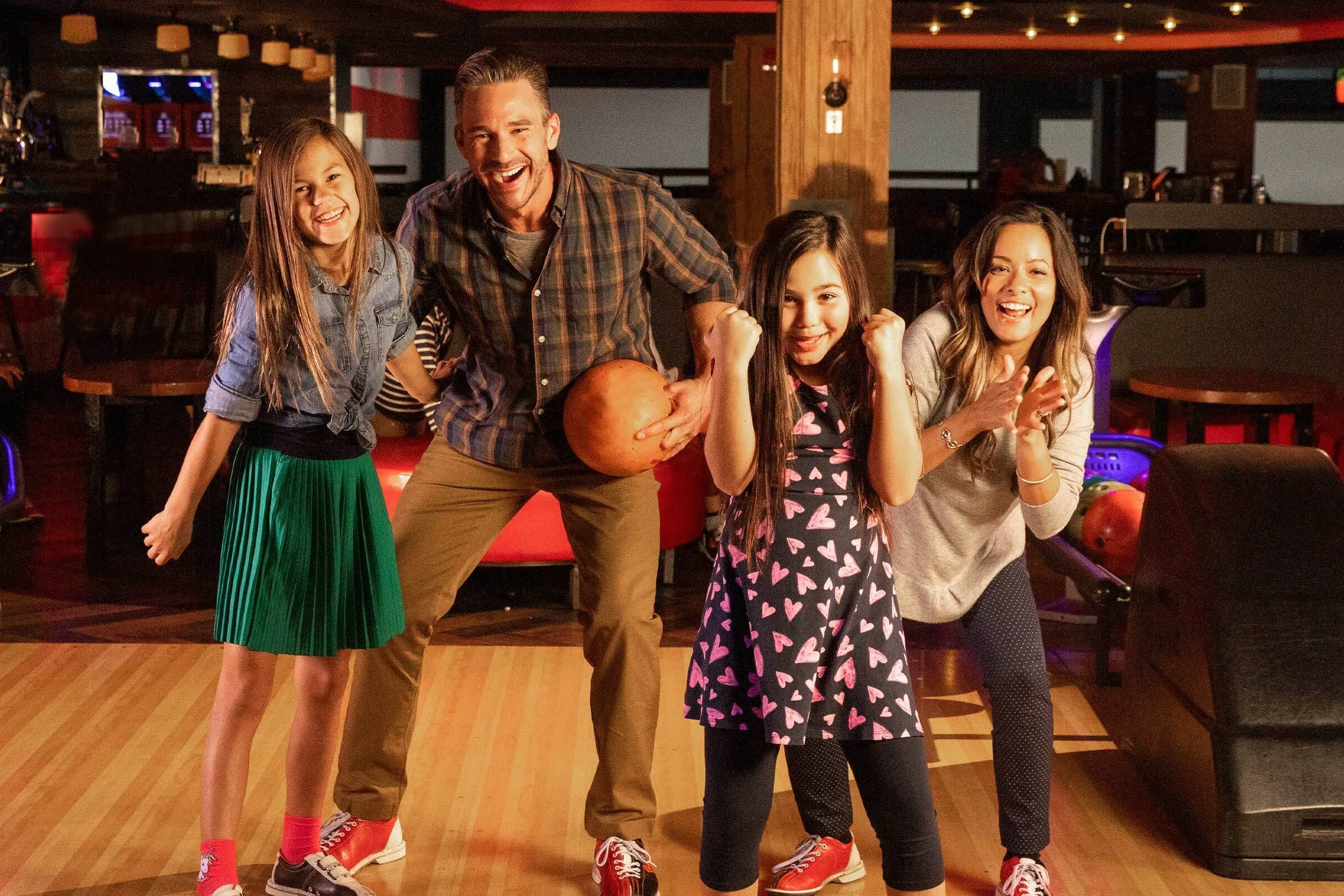 A family bonding on the lanes holding bowling balls and cheering each other on.