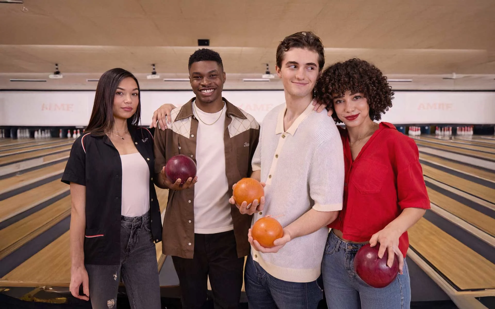 Group of friends holding duckpin bowling balls at a modern bowling alley with narrow lanes and duckpin pins in the background.