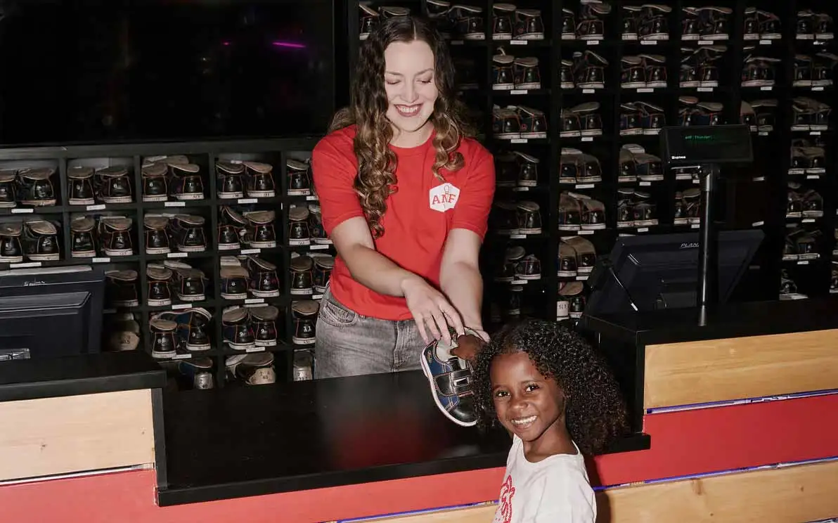 AMF staff member handing rental bowling shoes to a smiling young girl