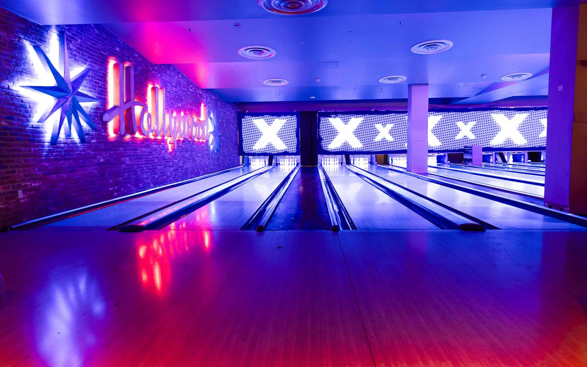 Modern bowling lanes with glowing neon “Hollywood” sign and illuminated pin decks inside an upscale Lucky Strike bowling alley.