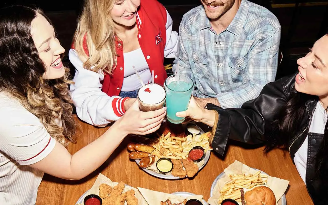 Friends sharing appetizers, burgers, fries, and cocktails at AMF Bowling, enjoying great food, drinks, and a social bowling night together.