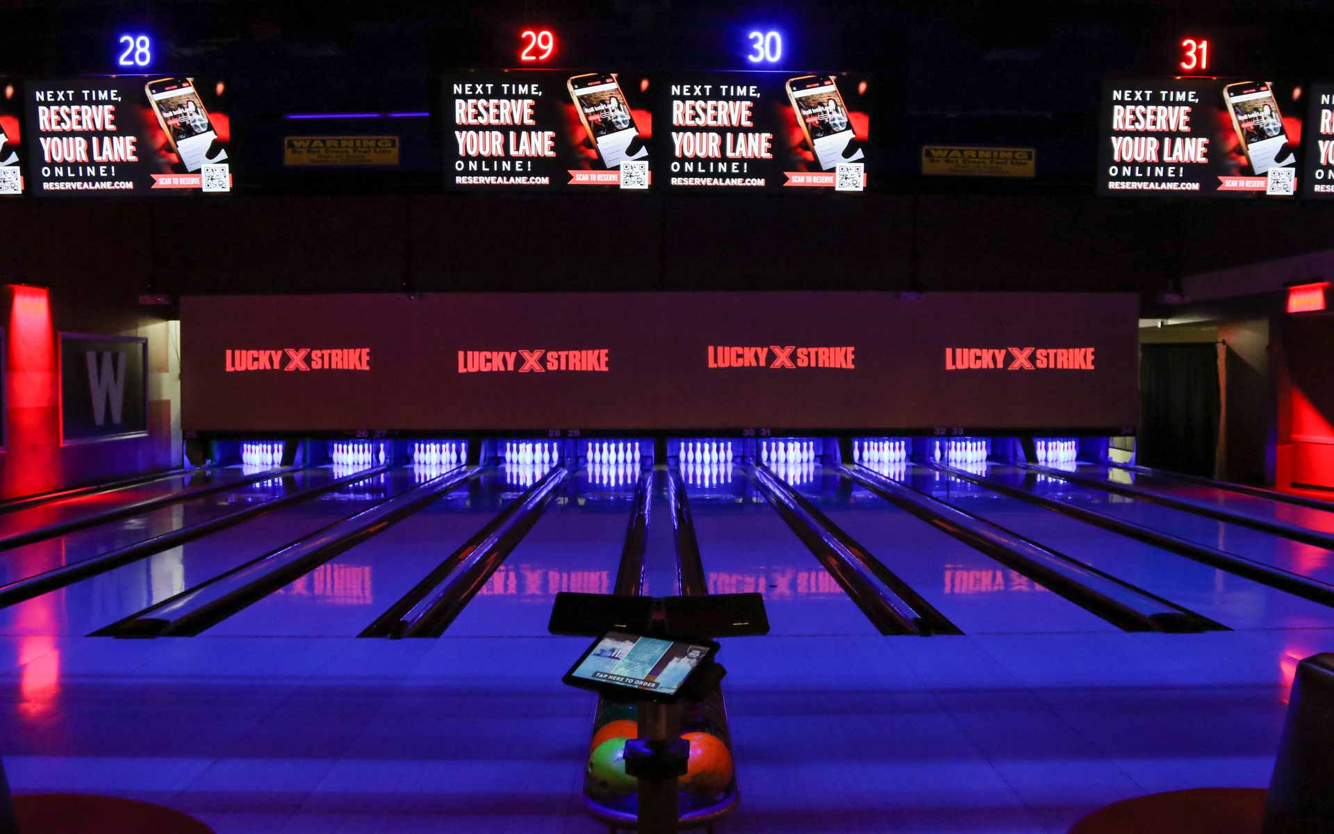 Polished bowling lanes with glowing pins, overhead scoring screens, and Lucky Strike signage in a dark, neon-lit environment
