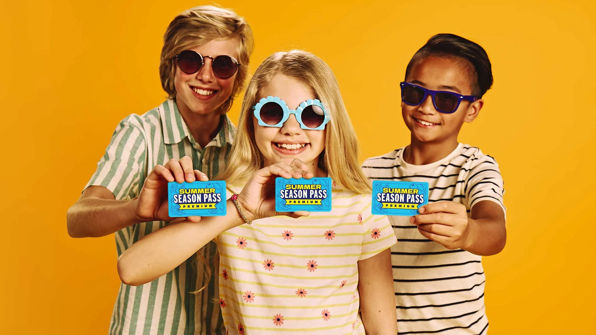 Three kids holding premium Summer Season Passes with a yellow background