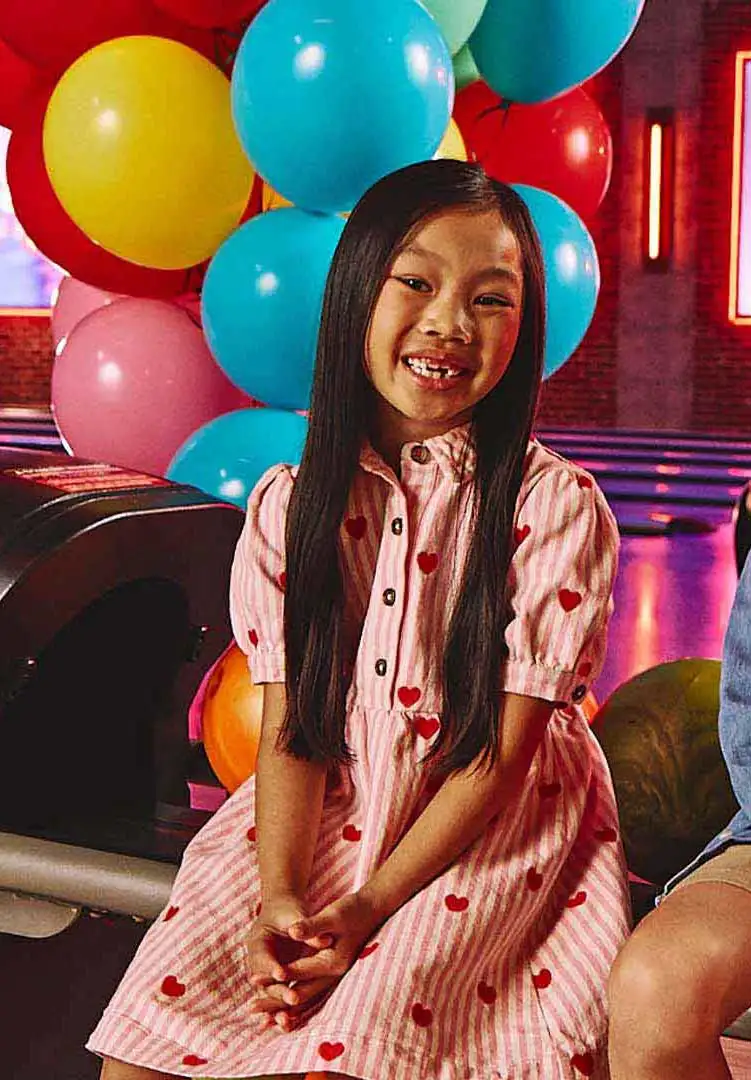A girl sitting by a bowling alley with party balloons in the background