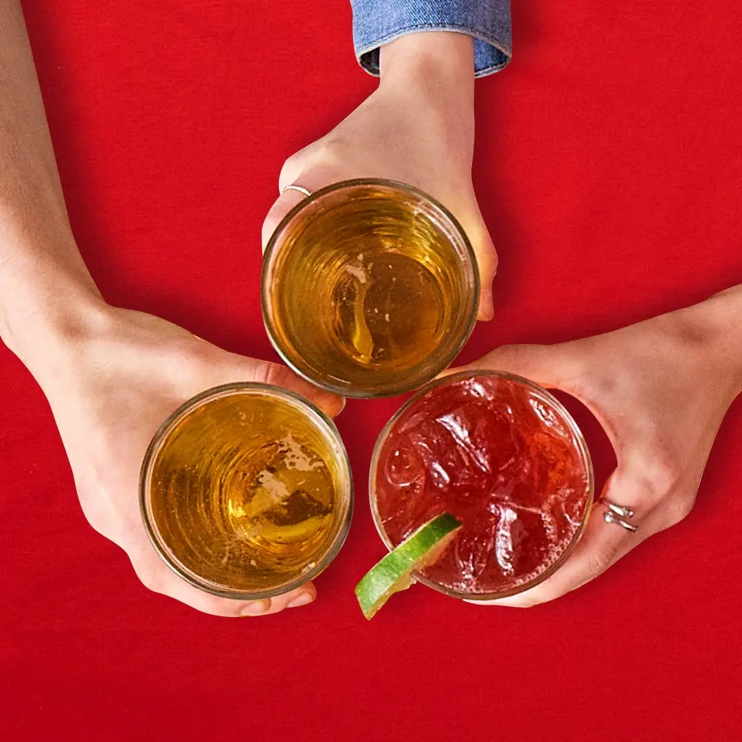 Three drinks in a cheers over a red holiday-themed table