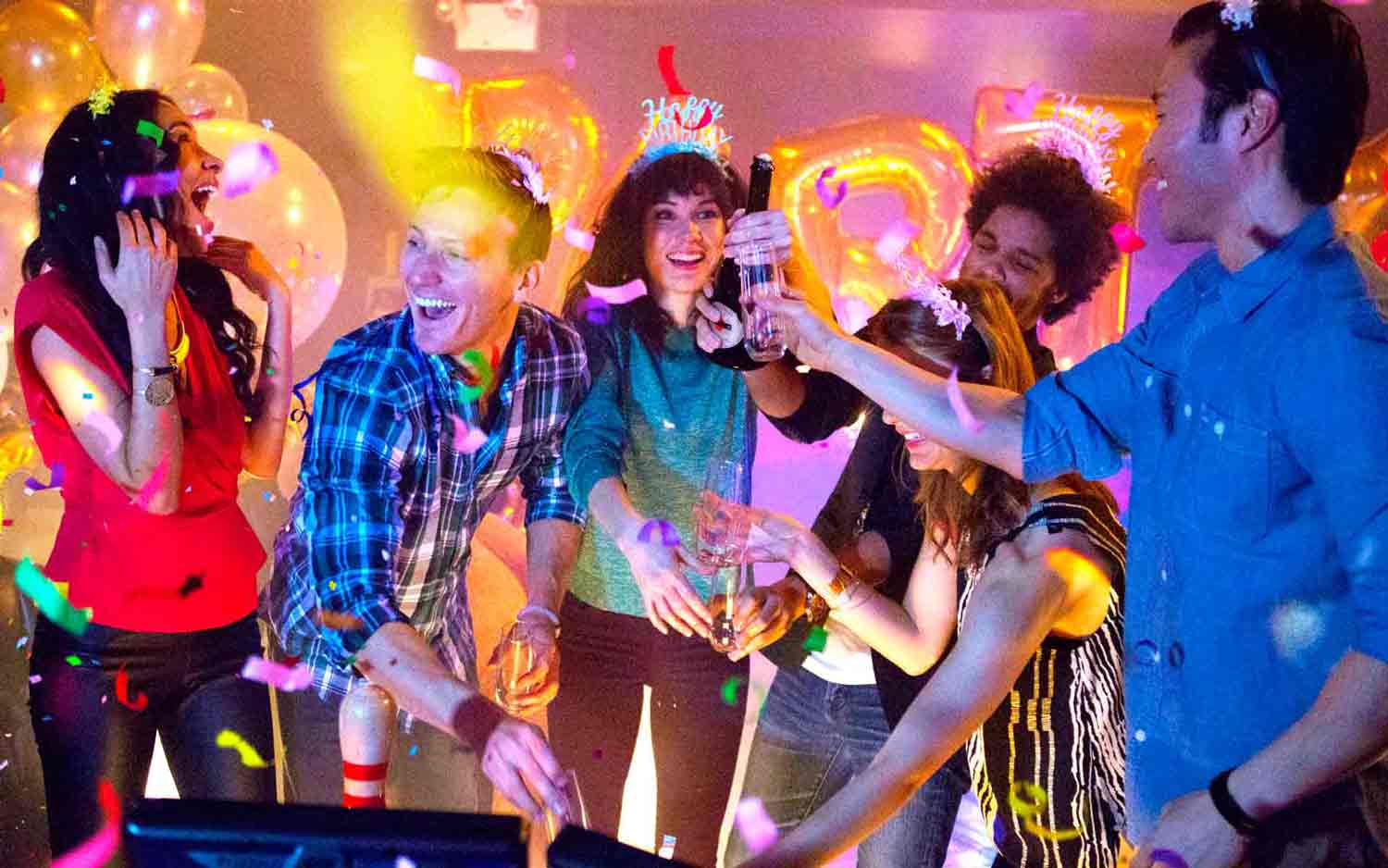 Friends celebrate a birthday party with confetti, champagne, and neon lights at a lively entertainment venue.