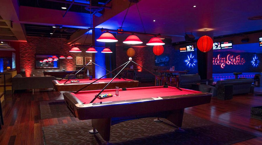 Lucky Strike billiards lounge with red felt pool tables, pendant lighting, wood floors, and bowling lanes visible in the background.