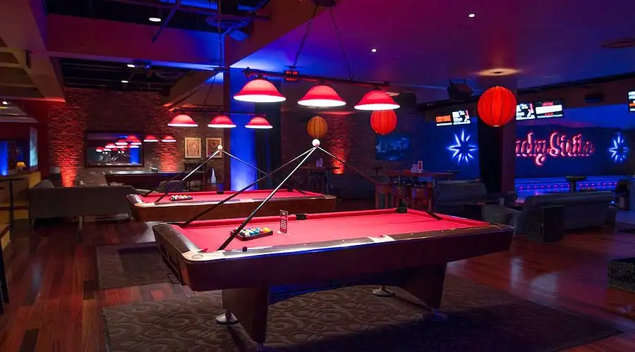 Lucky Strike billiards lounge with red felt pool tables, pendant lighting, wood floors, and bowling lanes visible in the background.