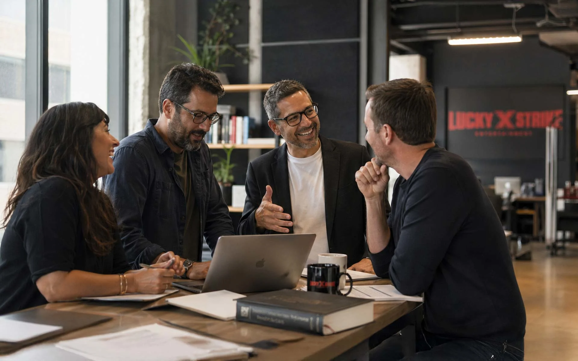 Team collaboration in modern corporate office at Lucky Strike Entertainment, employees discussing ideas around a laptop in an industrial open workspace.