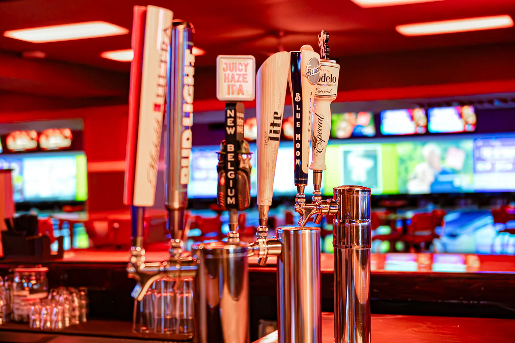 Multiple beer taps with bowling center and TV screens in the background