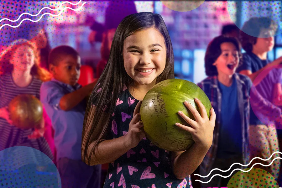 A girl holding a bowling ball and smiling with other kids in the background