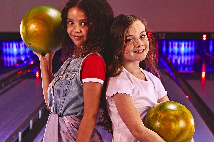 A girl holding a bowling ball and smiling with other kids in the background