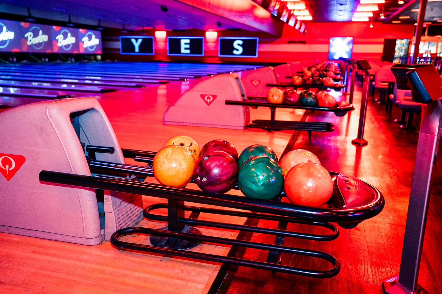 Colorful bowling balls on return rack with bowling center in the background.