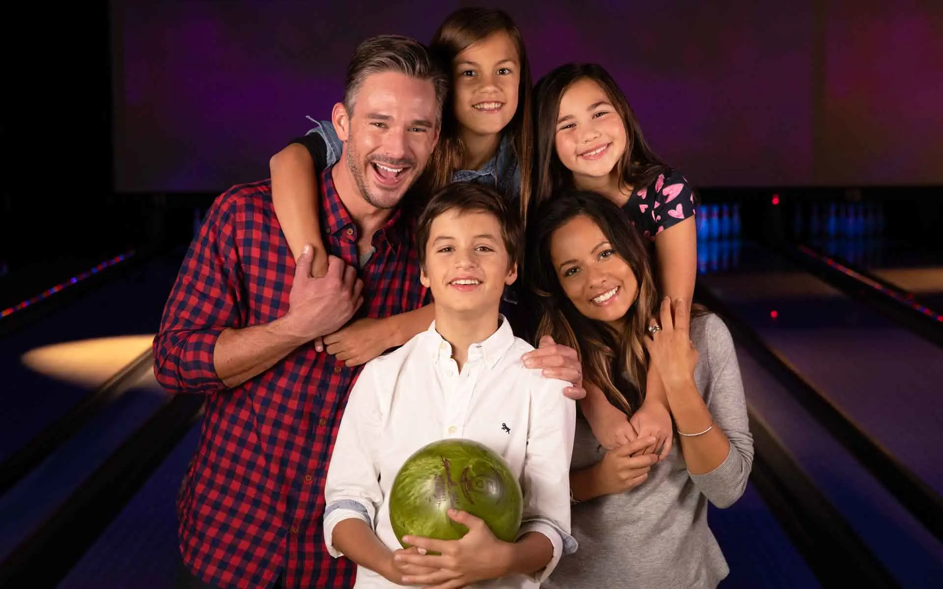 Happy family of five celebrating Father's Day at bowling center with dad holding bowling ball