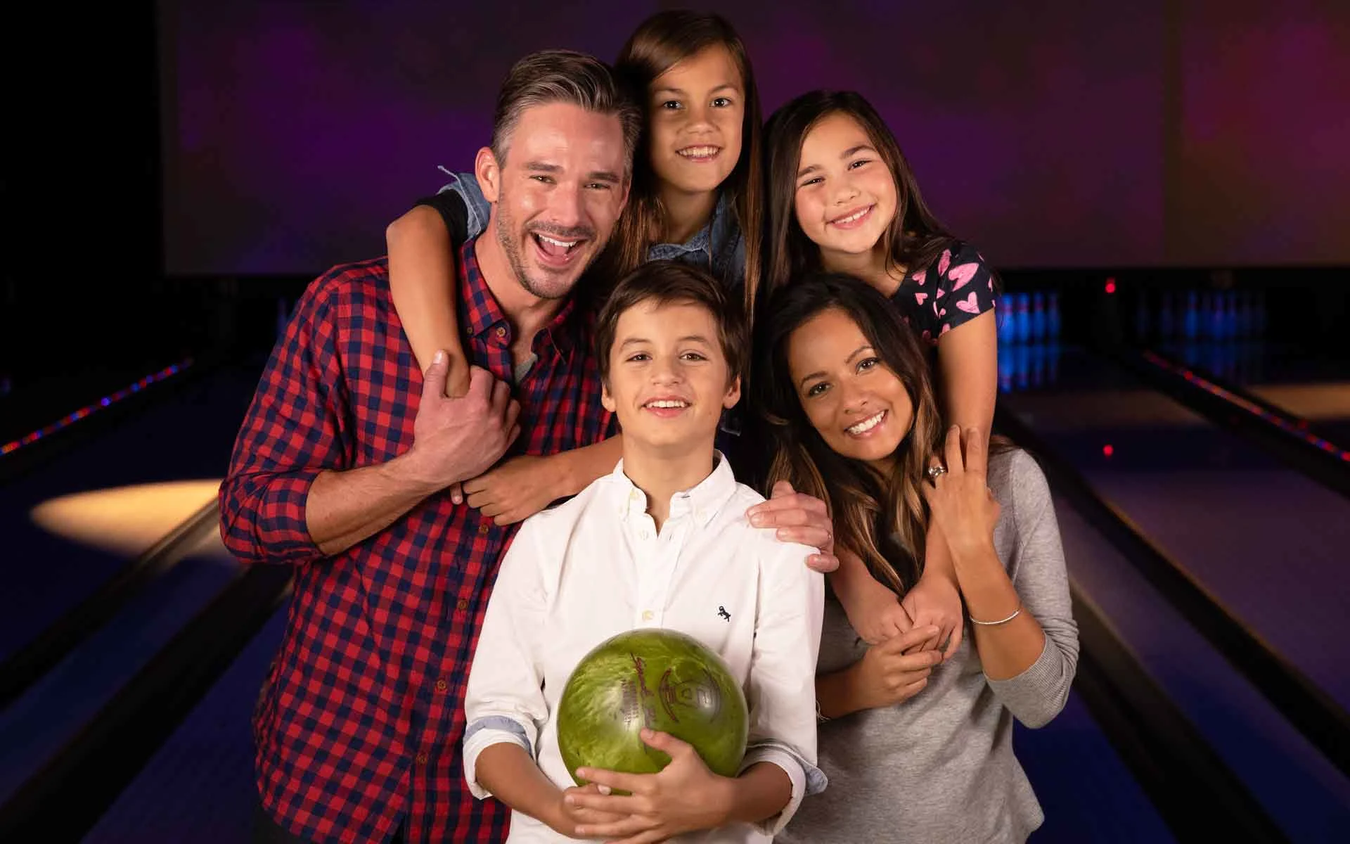 Happy family of five celebrating Father's Day at bowling center with dad holding bowling ball
