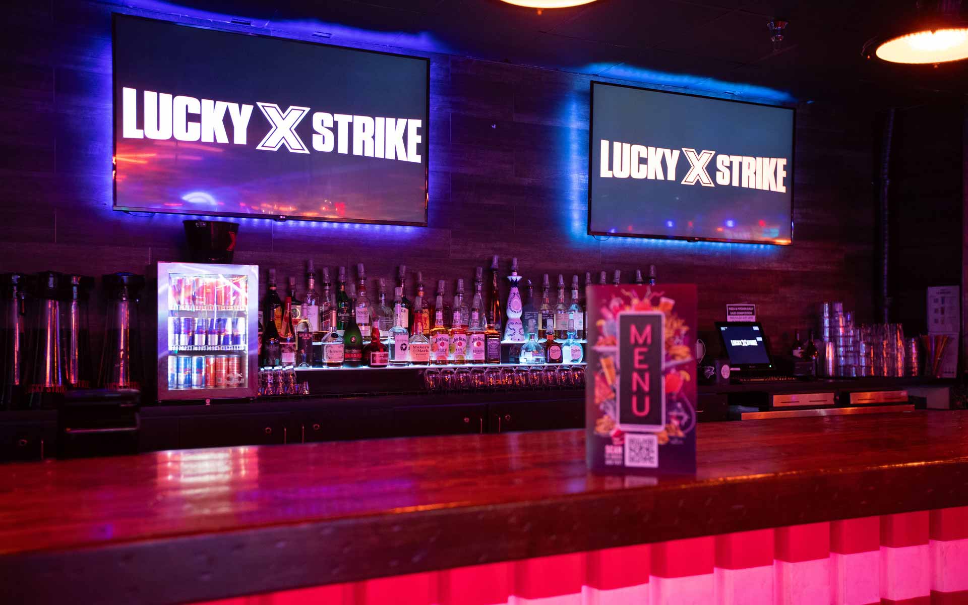 Lucky Strike bar with liquor display, digital menu screens, and ambient neon lighting in an upscale lounge setting.