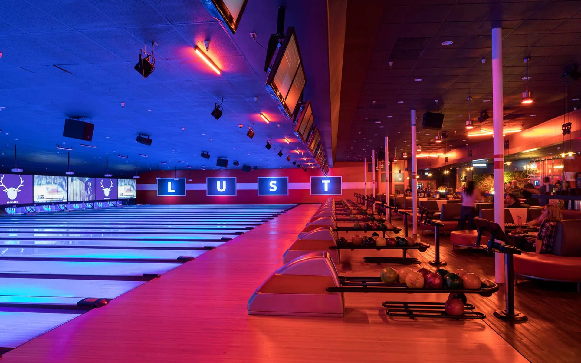 Expansive bowling alley with glowing neon lanes, overhead scoring screens, and a vibrant lounge area, featuring bold lighting and a lively, modern entertainment atmosphere.