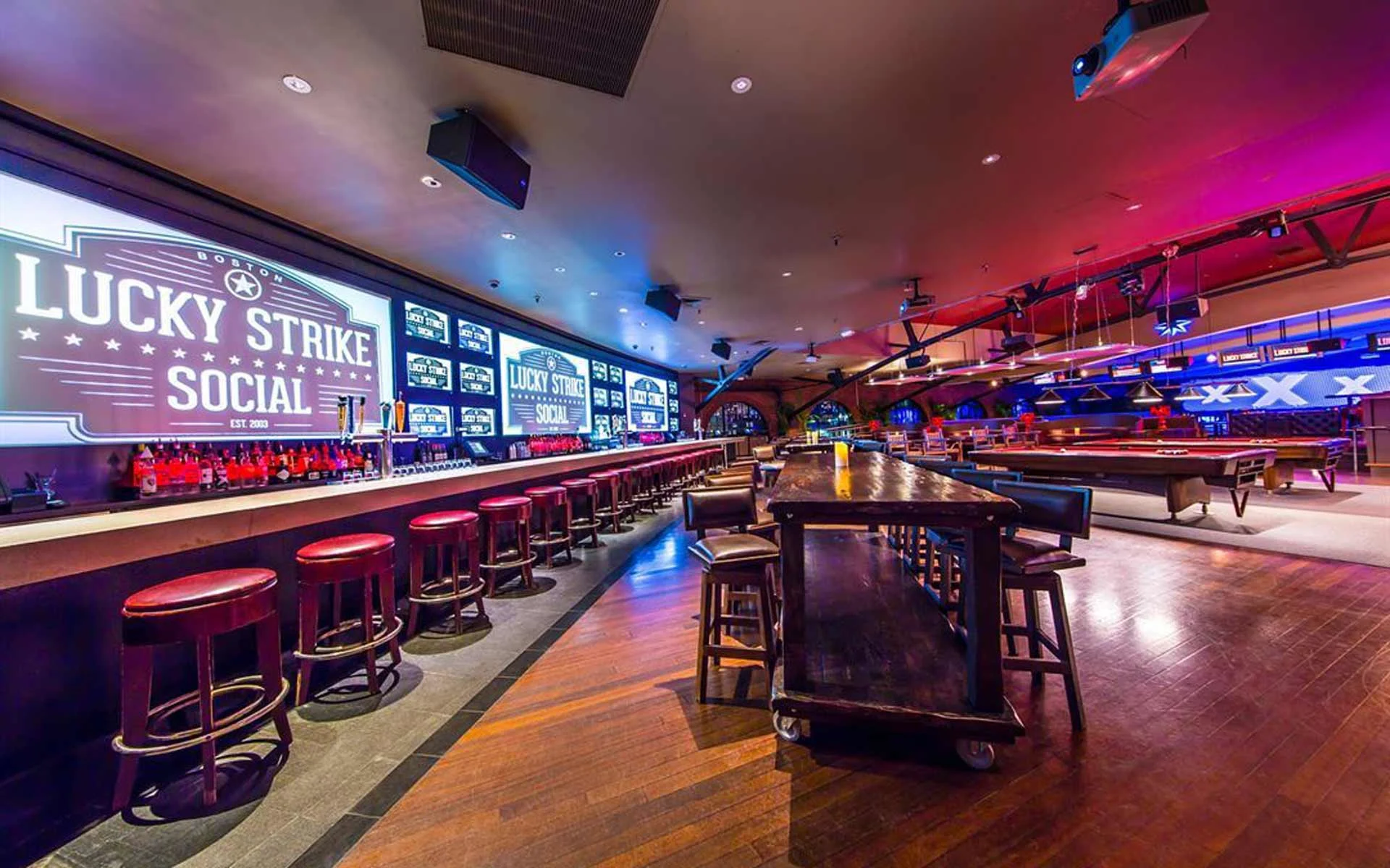 Modern Lucky Strike Social bar with large illuminated branding, bar seating, and open lounge space with billiards tables in the background.