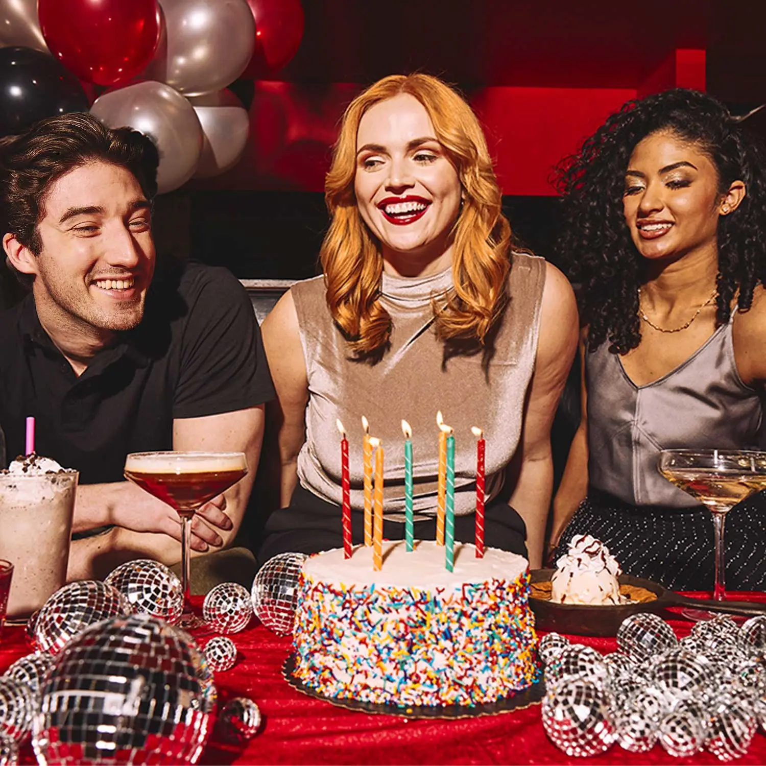 Three people sitting behind a birthday cake with candles.