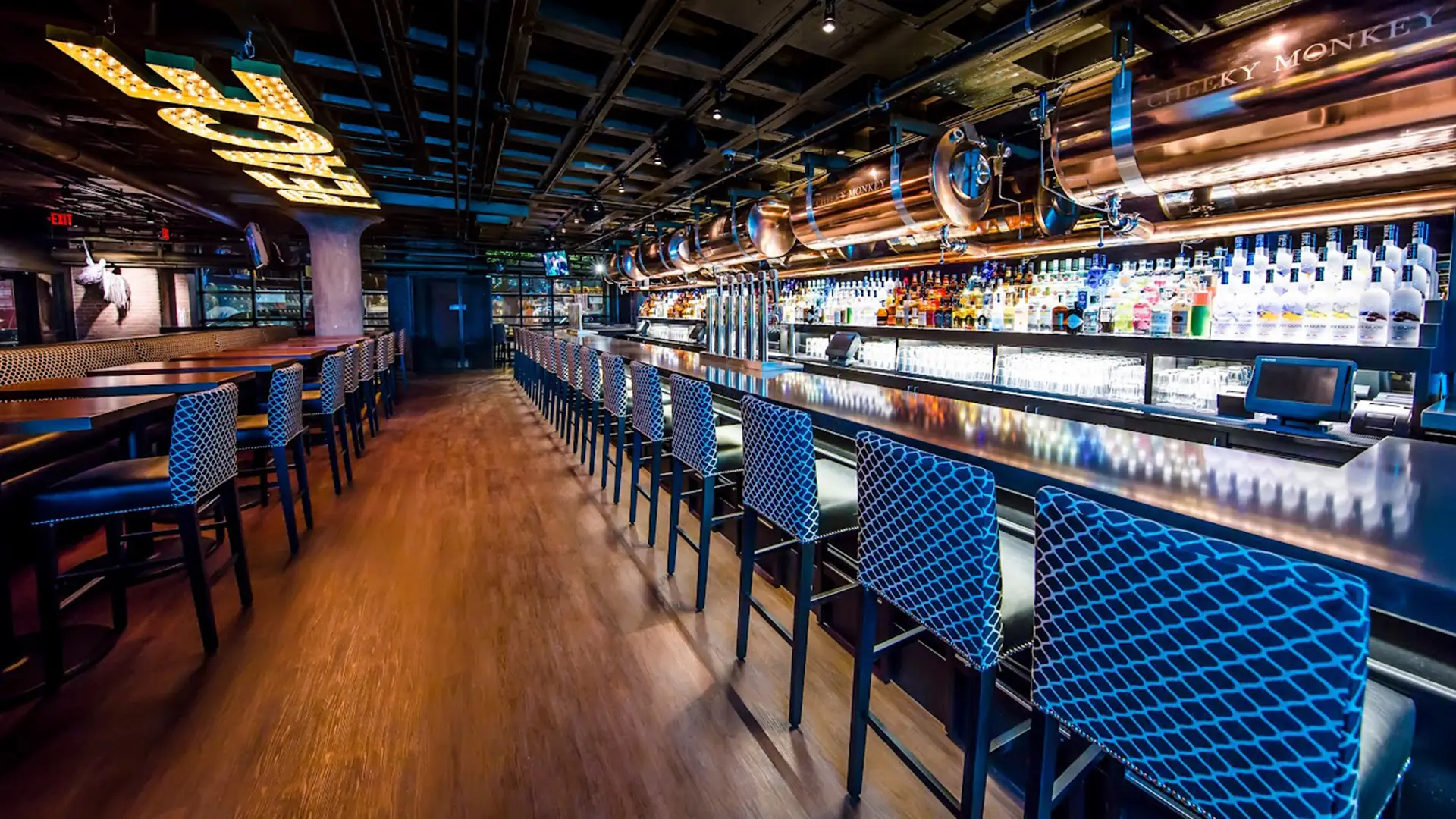 Cheeky Monkey bar with long counter seating, illuminated beer tanks, and a full liquor display.