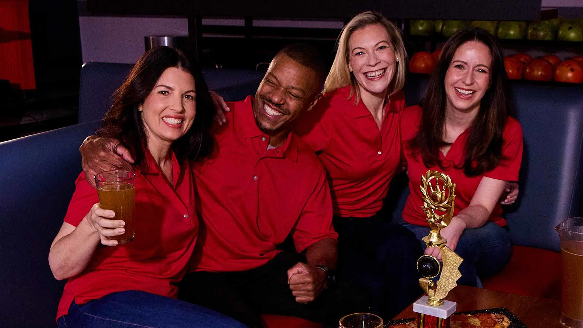 Bowling league teammates celebrating with drinks and a trophy in a lounge area at the bowling alley