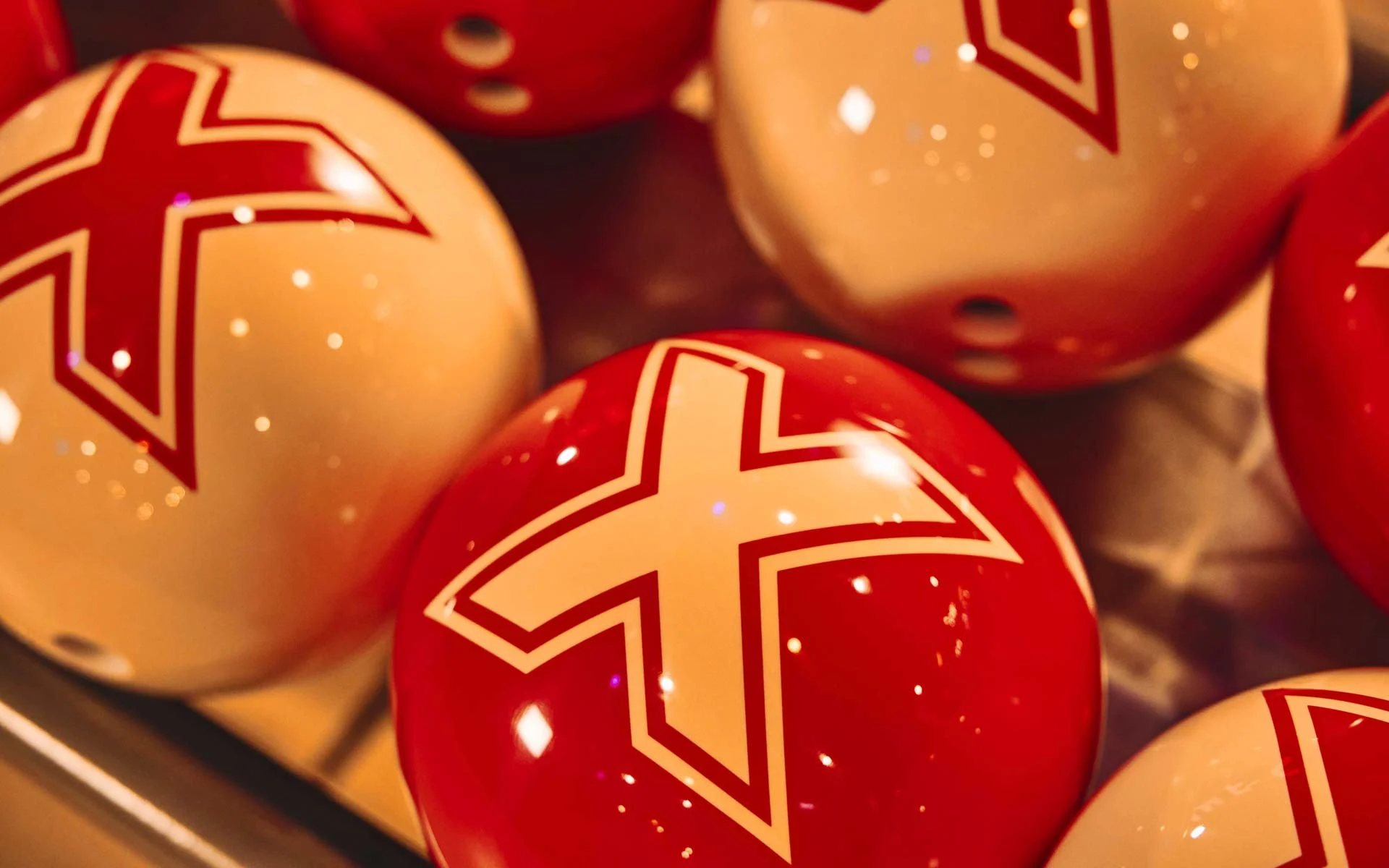Close-up of red and cream bowling balls featuring the Lucky Strike “X” logo on a ball return.