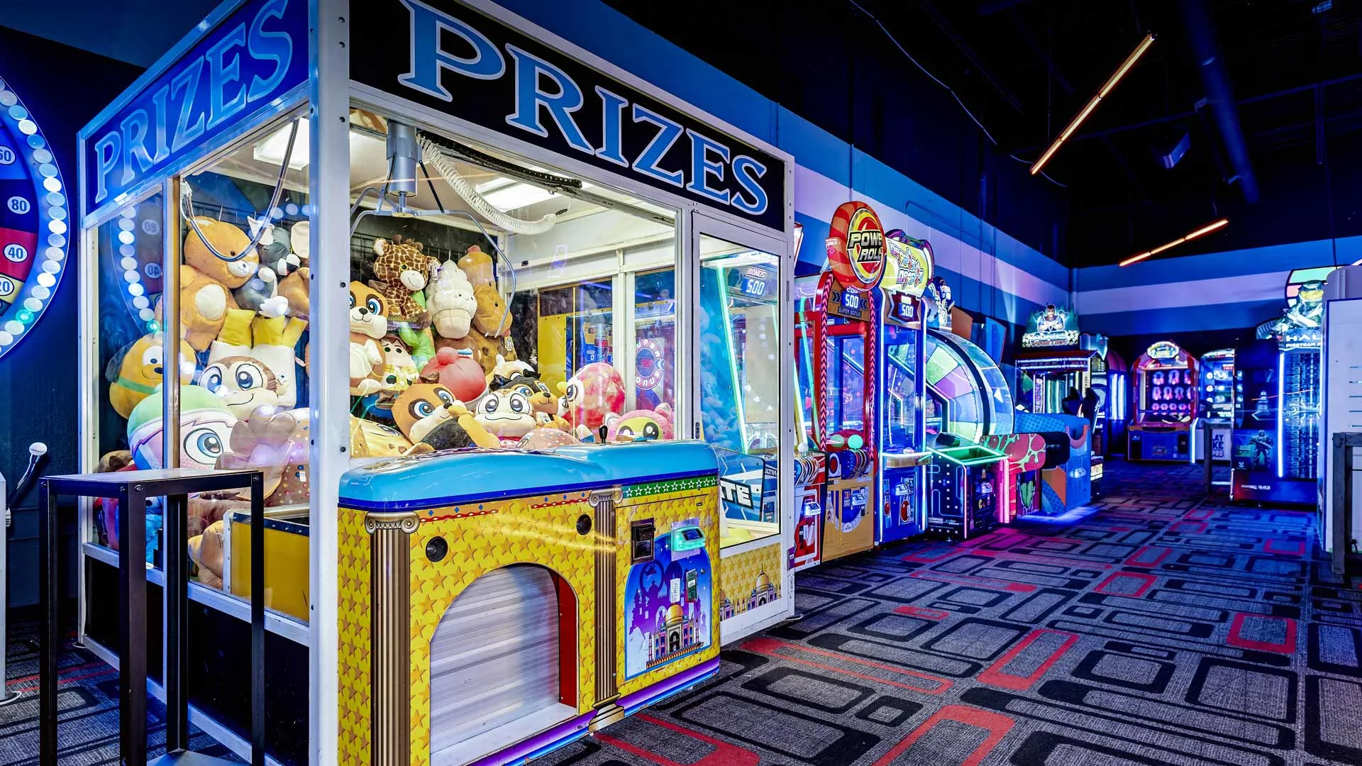 Arcade prize section at Lucky Strike with a large claw machine filled with plush toys and a row of illuminated arcade games.