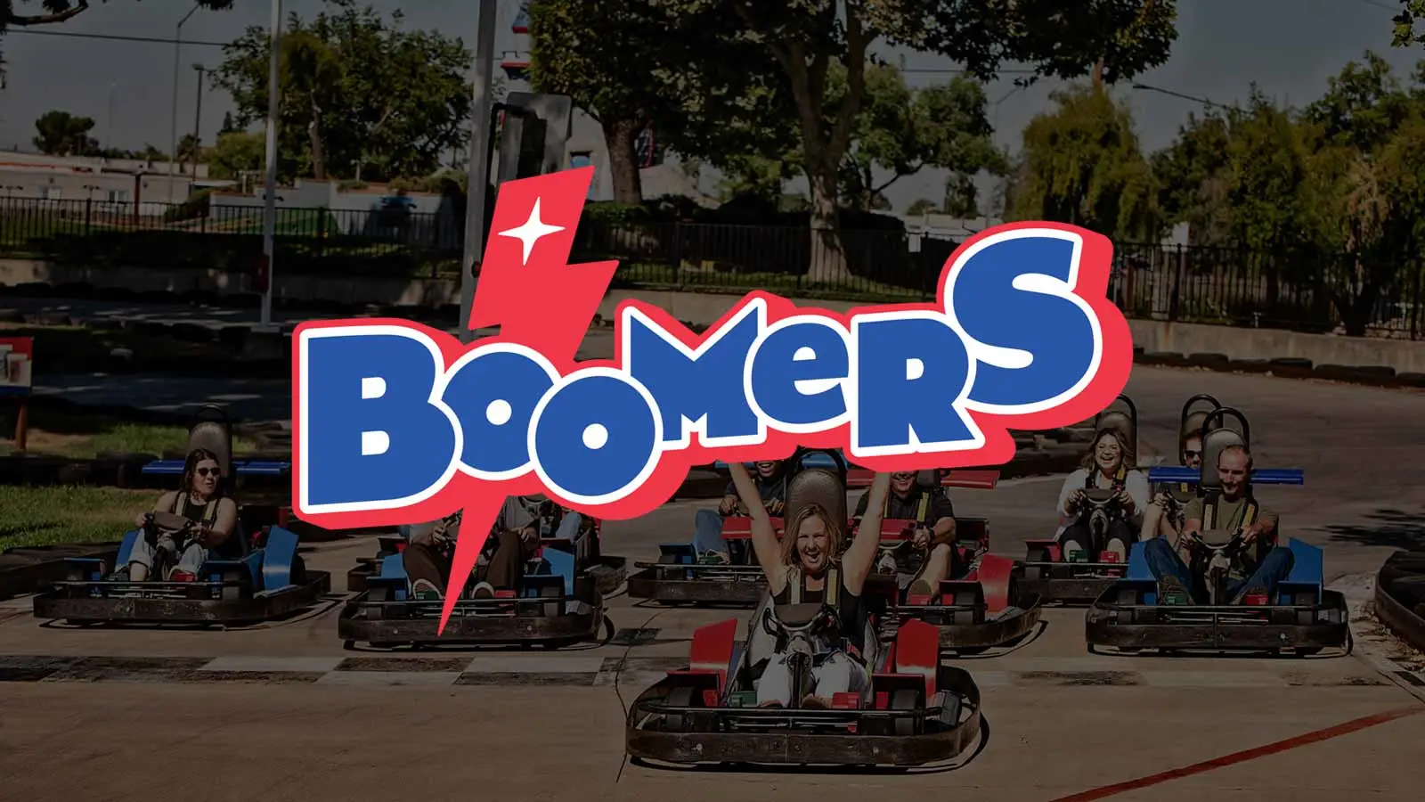 Boomers logo over a go-kart track with riders racing outdoors, arms raised in excitement.