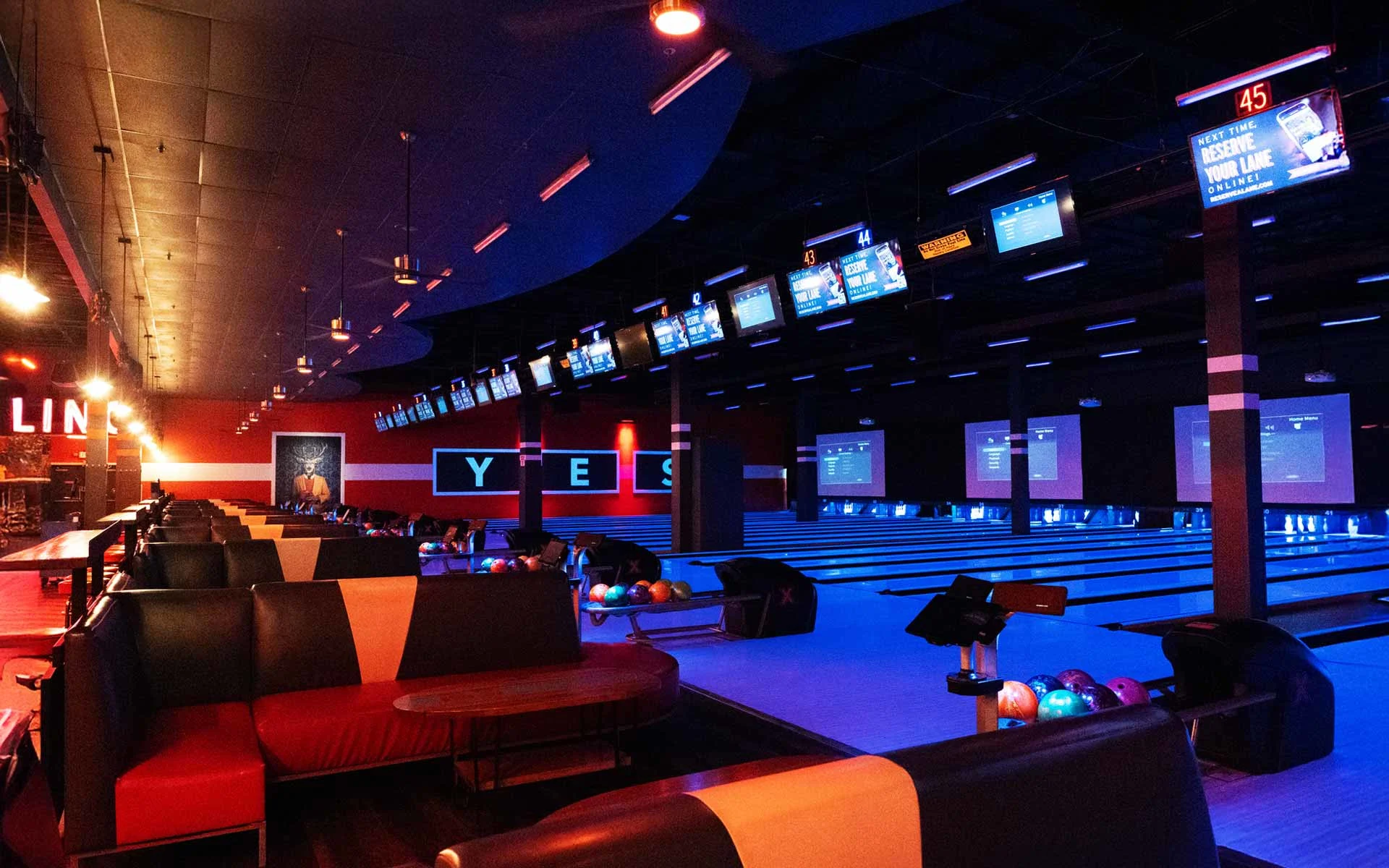 Modern Lucky Strike bowling lanes with neon blue and red lighting, leather lounge seating, overhead scoring monitors, and multiple polished lanes ready for play.