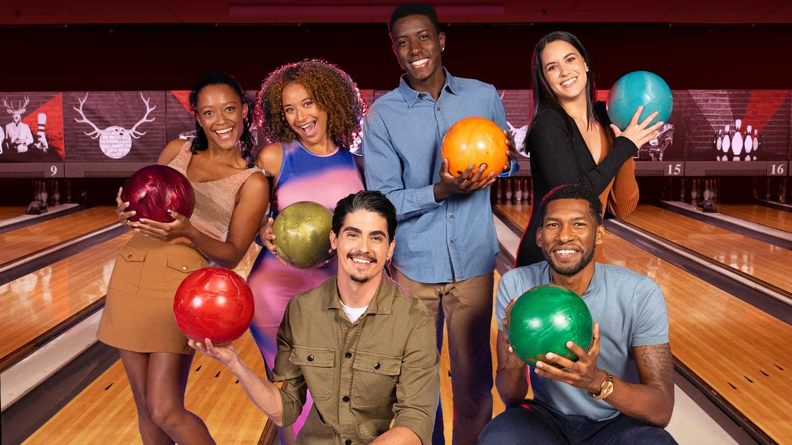 Group of friends holding bowling balls with bowling lanes in the background.