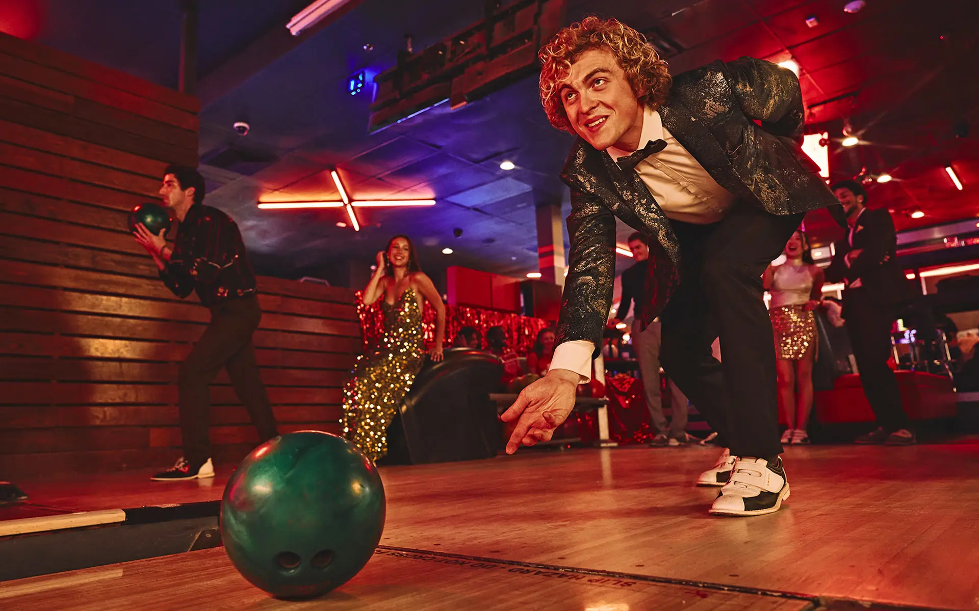 A man bowls in festive attire with friends in the background.