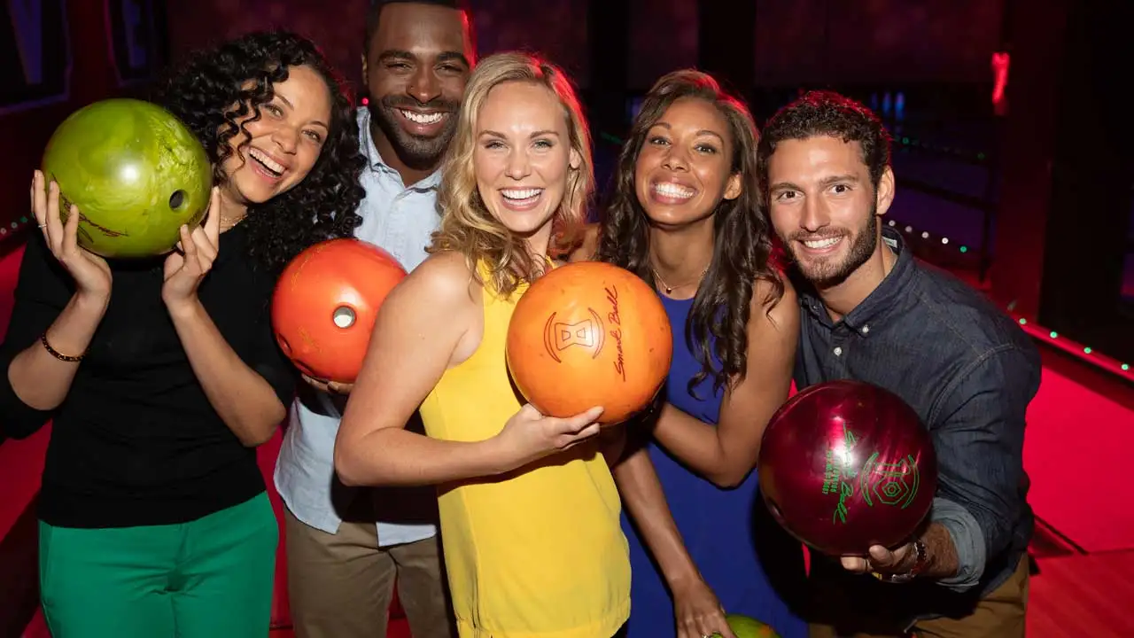 A group of friends posting in front of bowling lanes holding bowling balls.