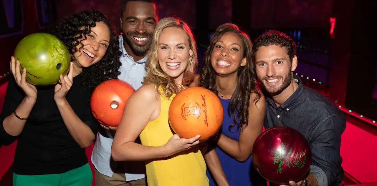 A group of friends posting in front of bowling lanes holding bowling balls.