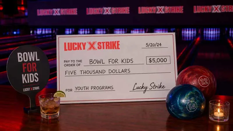 Lucky Strike charity event with drinks, donation check, and moody red-purple lane lighting.