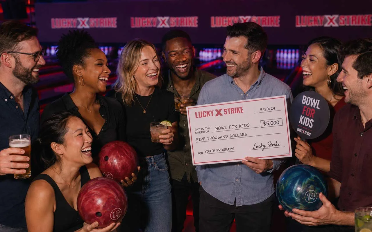 Diverse guests laugh, bowl, and raise funds at a Lucky Strike charity event with drinks, donation check, and moody red-purple lane lighting.