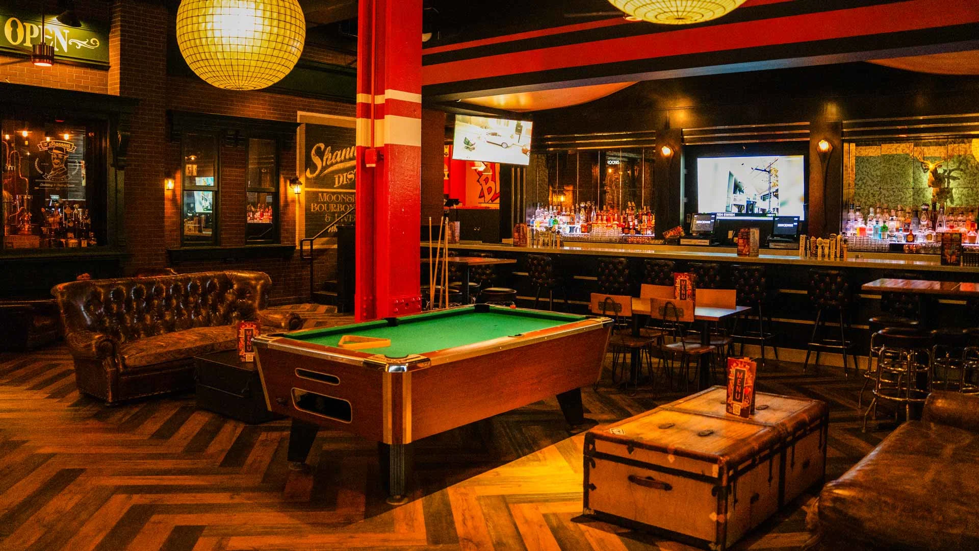 Upscale bowling lounge interior with a pool table, leather seating, and full bar with TVs and warm ambient lighting.