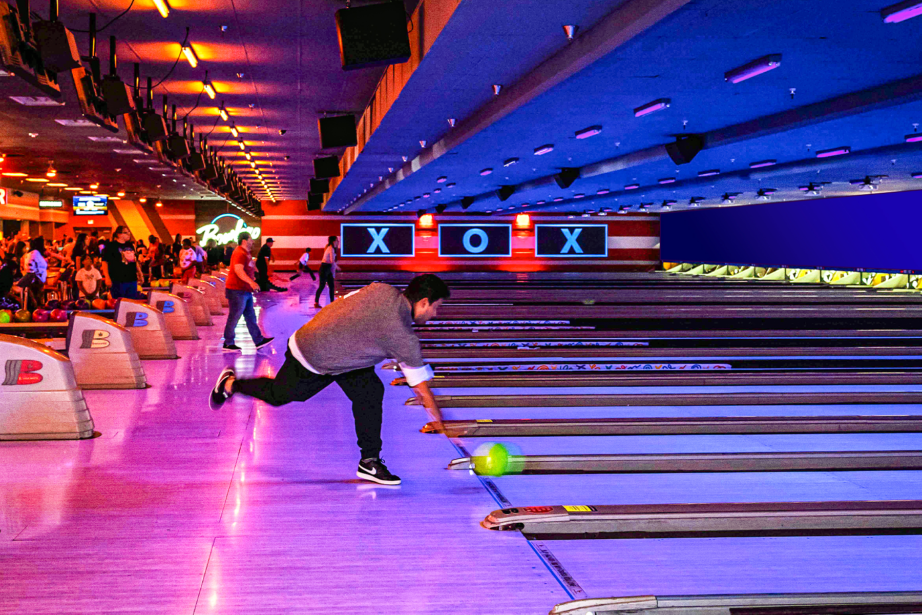 Person rolling bowling ball down black light bowling lane