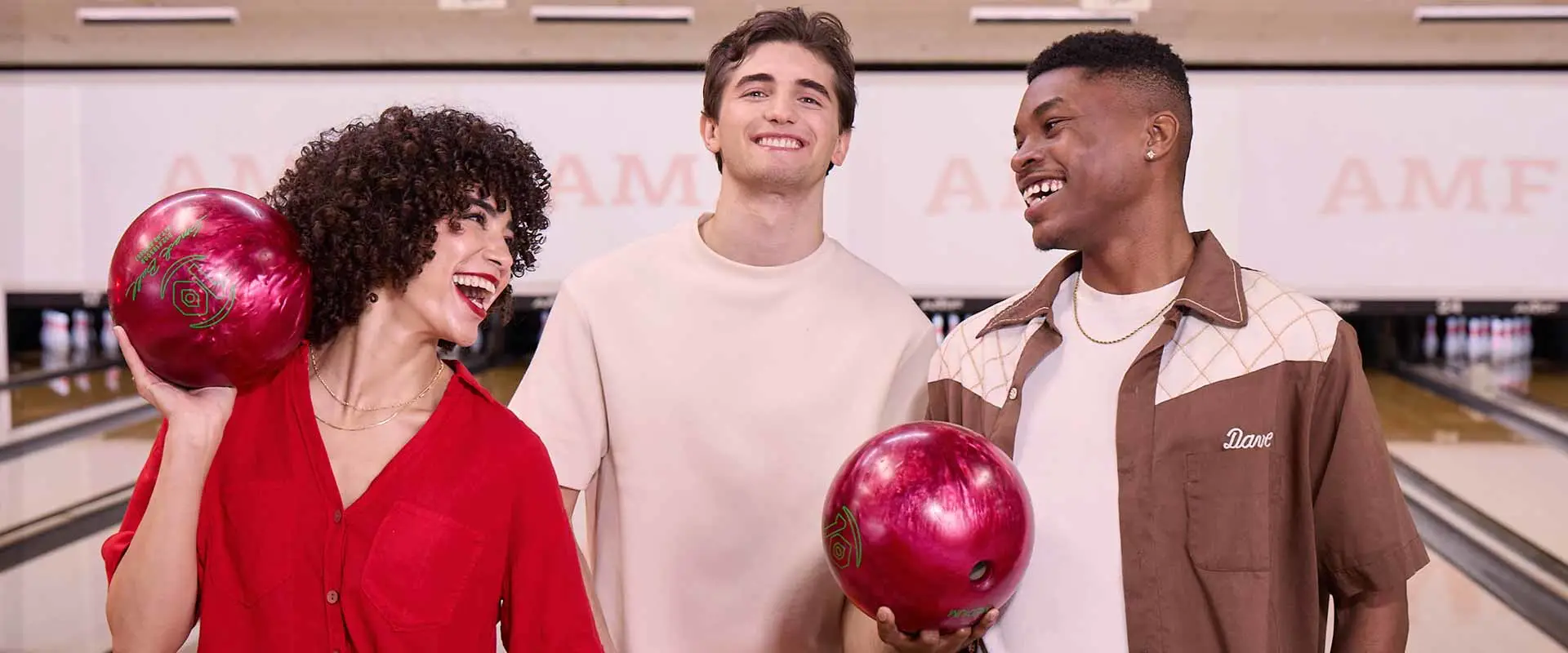 Three adults laughing together holding bowling balls at AMF Bowling lanes.