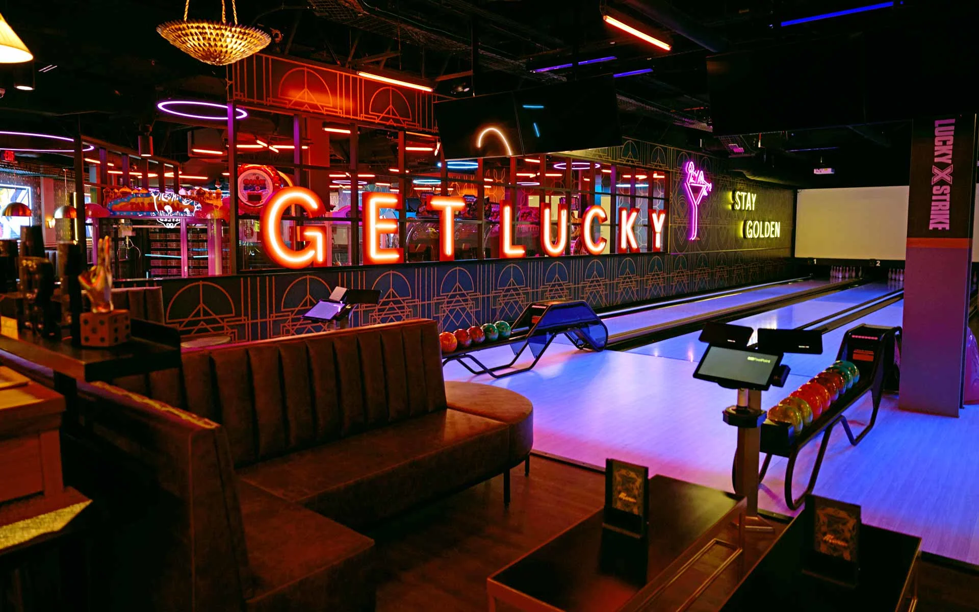 Upscale bowling alley interior with neon “Get Lucky” signage, glowing lanes, and modern lounge seating at a Lucky Strike venue, featuring vibrant nightlife lighting, ball returns, and an energetic entertainment atmosphere.